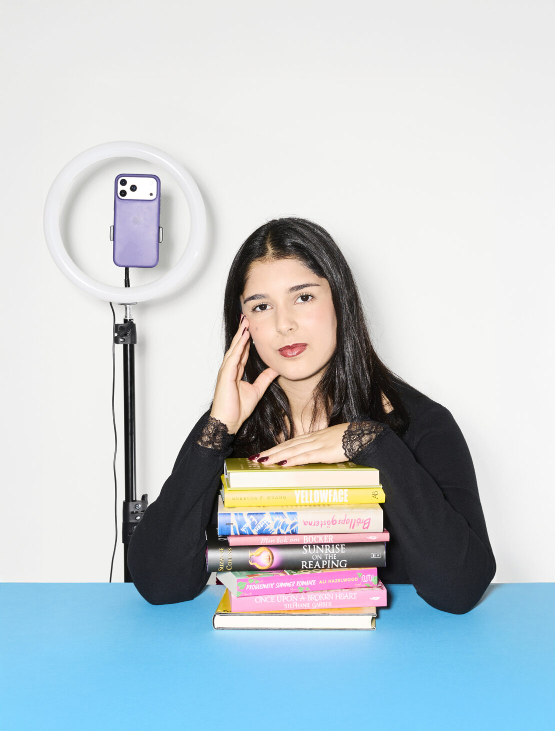 Porträttbild på Jasmine Darban med en trave böcker och mobilutrustning.