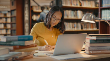 En person på ett bibliotek som studerar med böcker omkring sig.